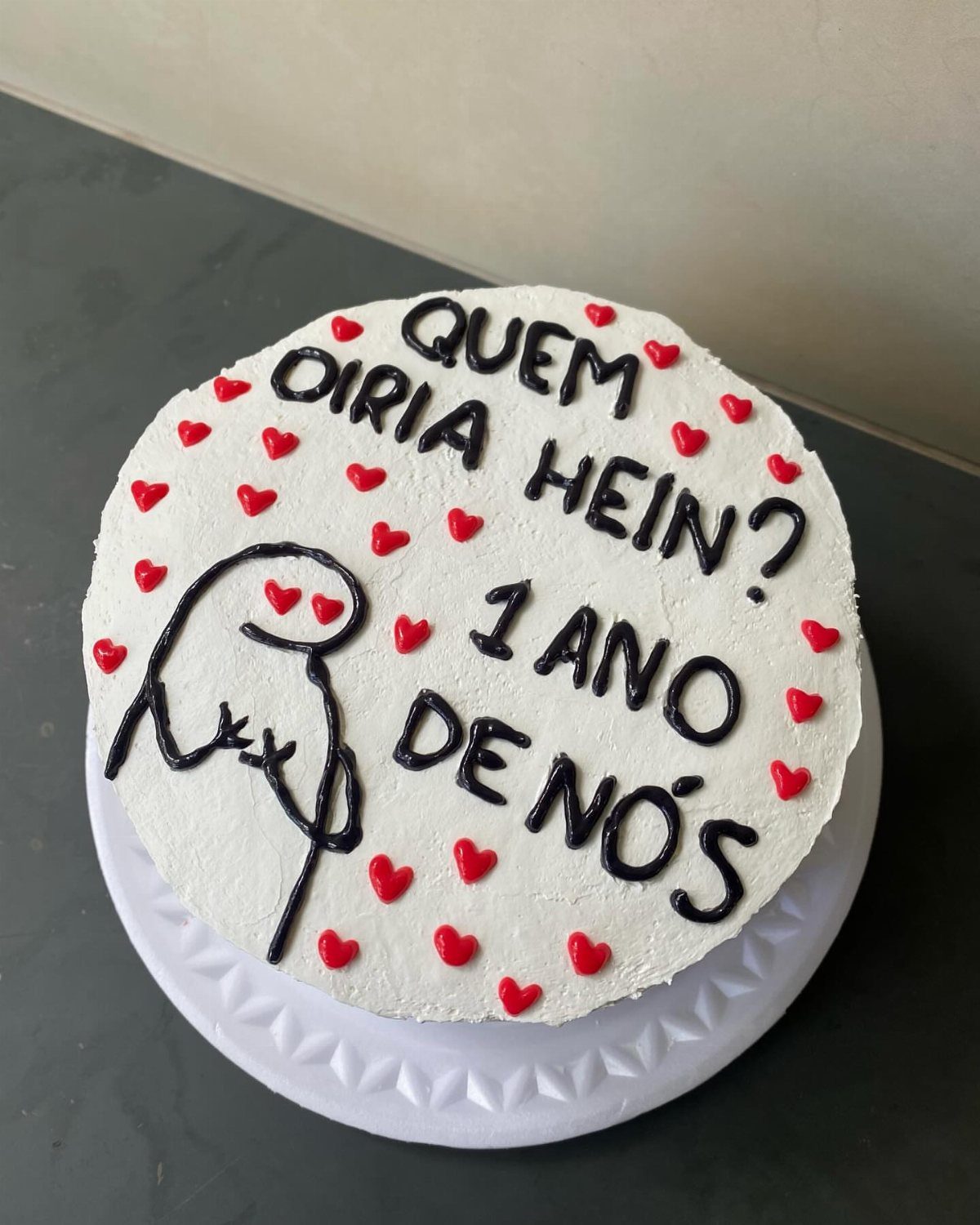 White frosted cake with red hearts and a hand-drawn icing couple hugging.