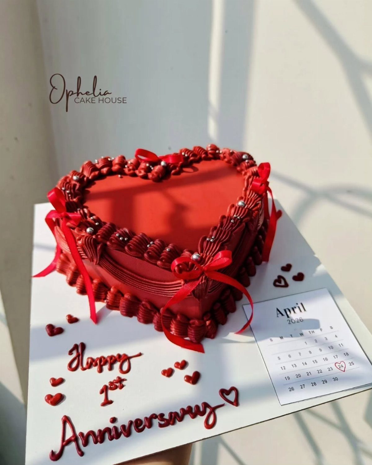 Red heart-shaped anniversary cake with ribbons and a small calendar on white board