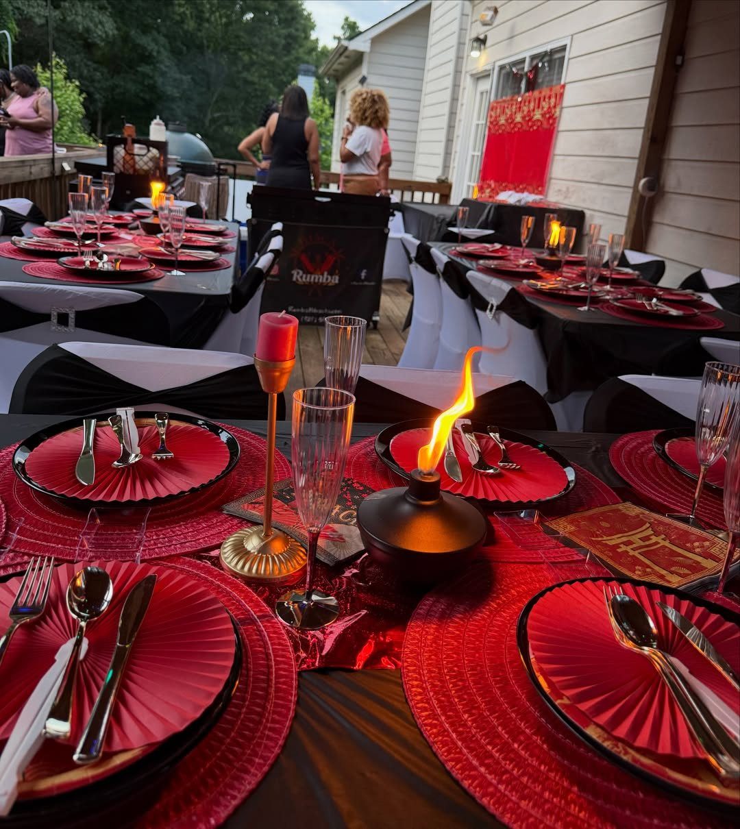 Formal outdoor dinner table with red plates, black tablecloths, and flaming centerpieces.