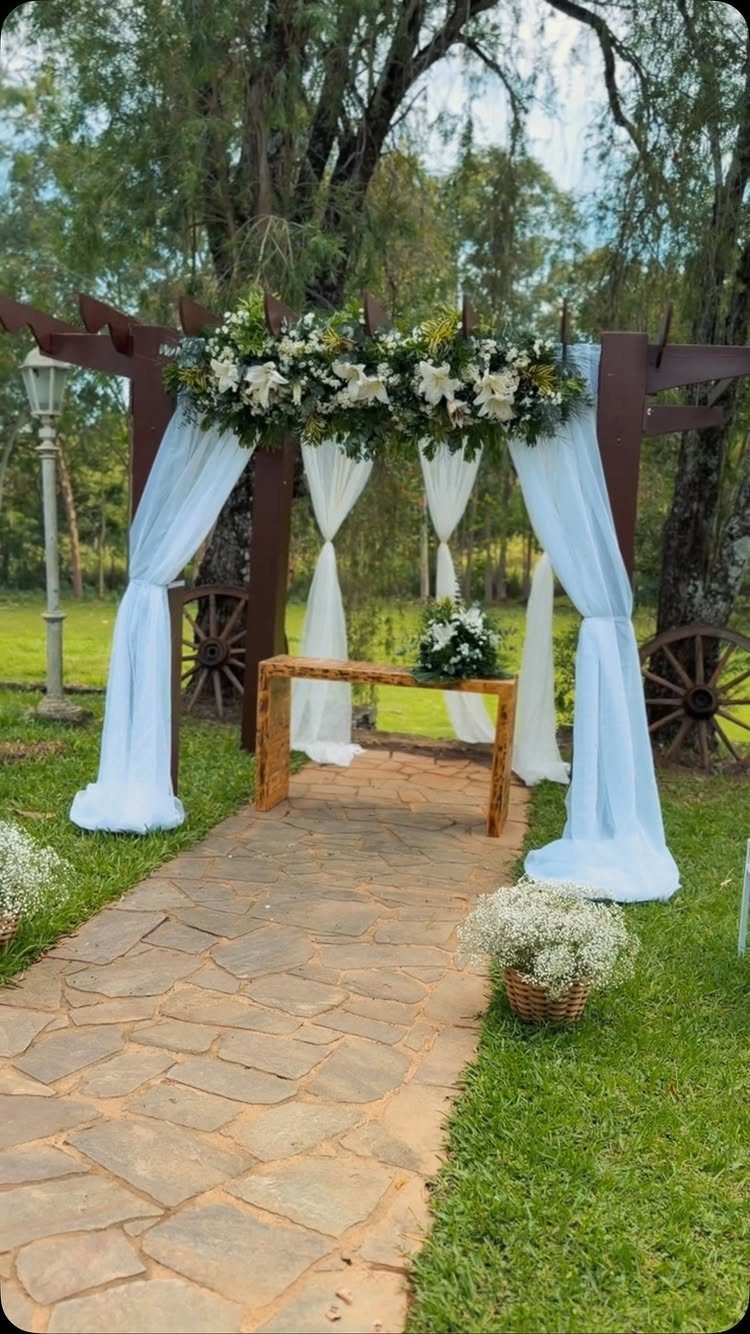 Wooden pergola with white fabric and lilies over a stone path in a garden