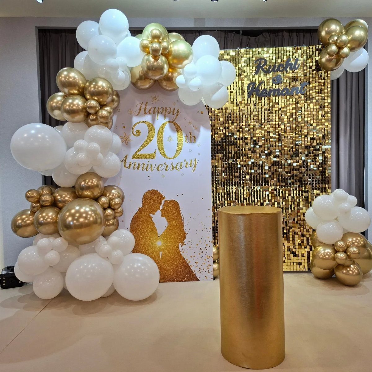 Gold and white balloon arch with 20th anniversary sign and sequin backdrop.