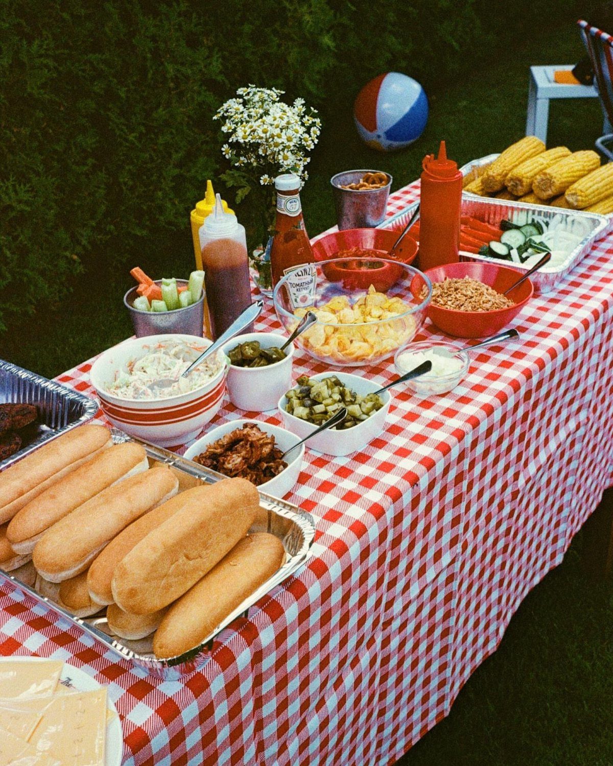 BBQ food spread on a red checkered tablecloth in an outdoor garden setting.