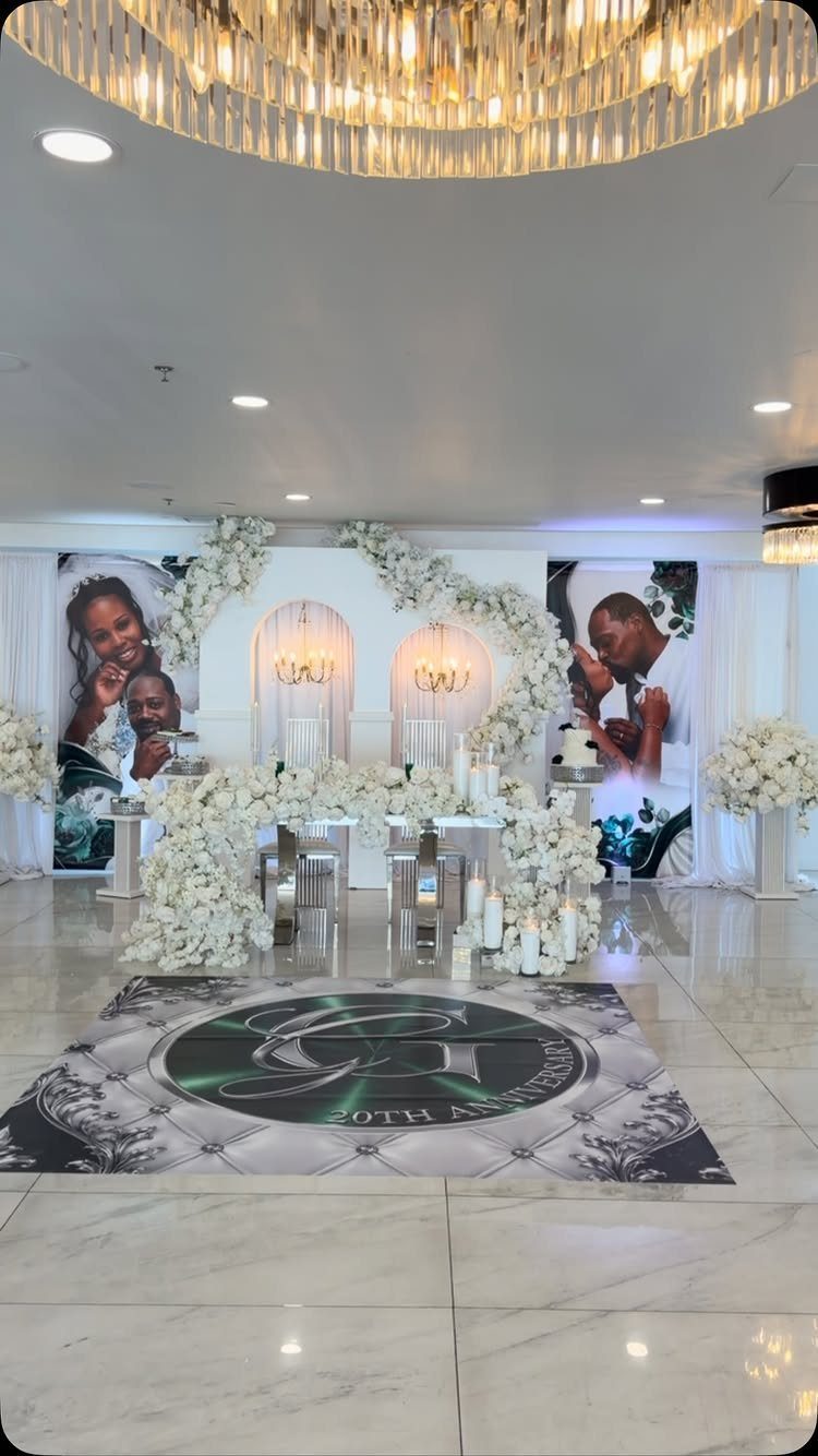 Elegant 20th anniversary party setup with white floral arches and couple portraits.