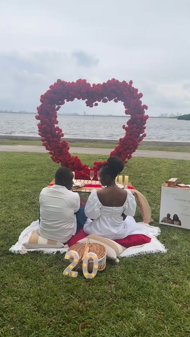Couple enjoying a romantic picnic with a large red heart floral backdrop and number 20.