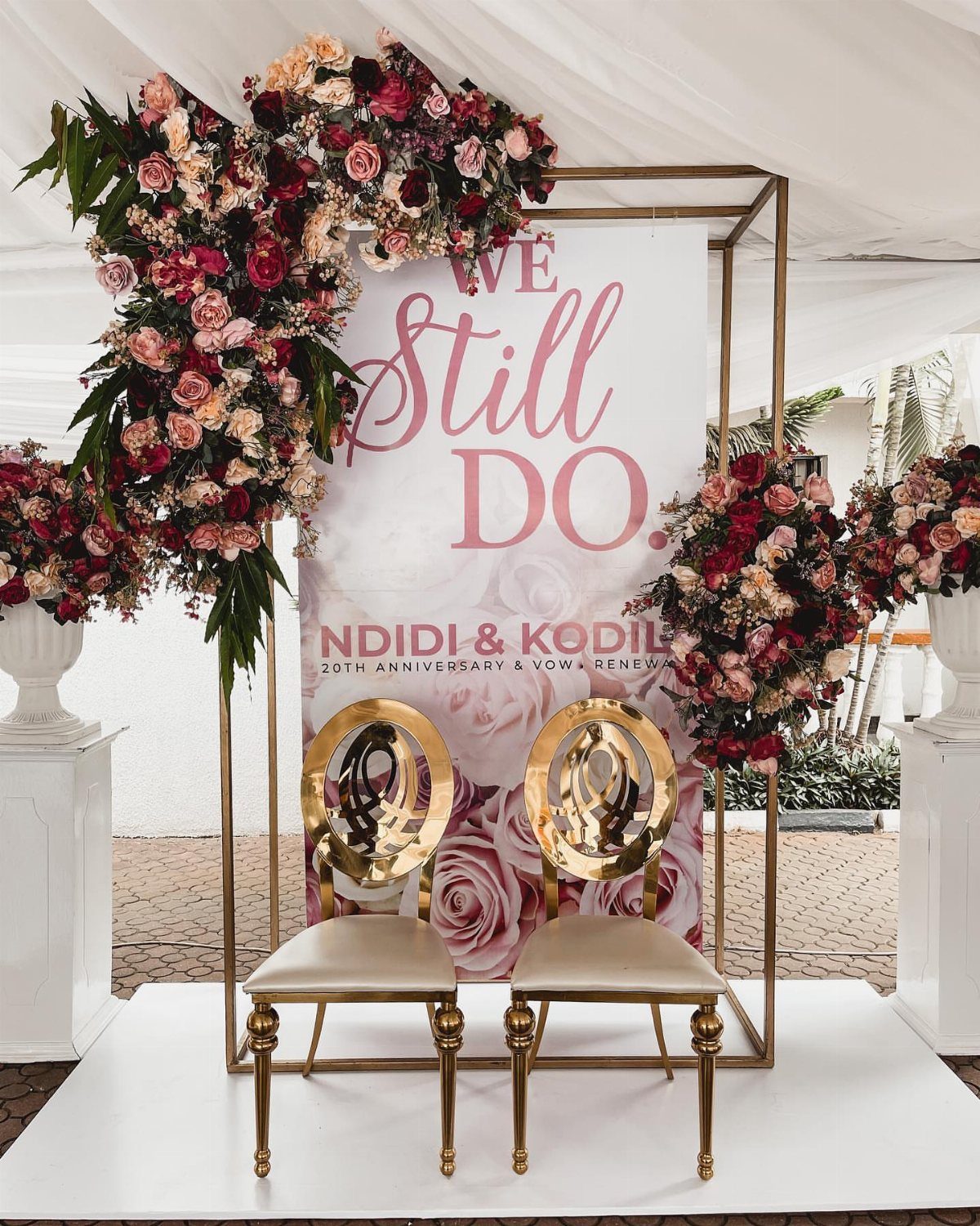 Gold frame backdrop with red roses and 'We Still Do' sign for vow renewal.
