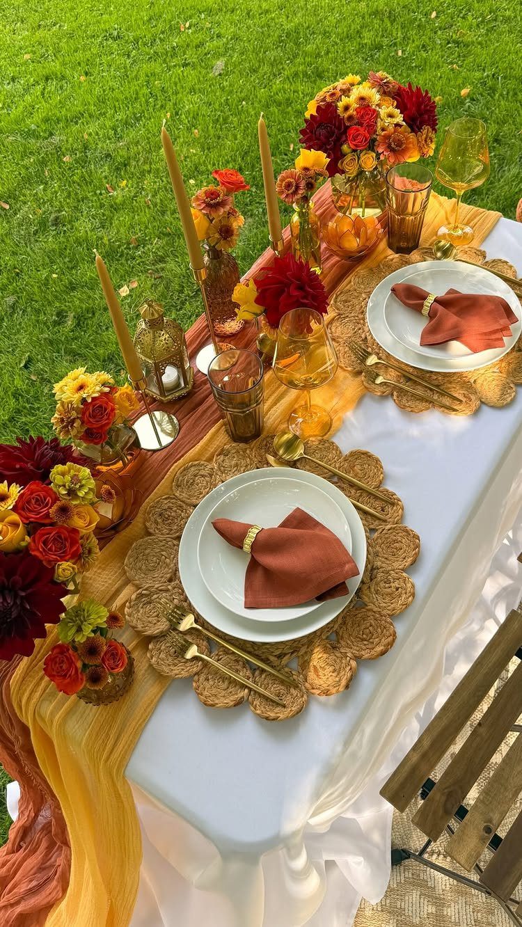 Elegant outdoor table setting with autumn-colored flowers, gold accents, and amber glassware.