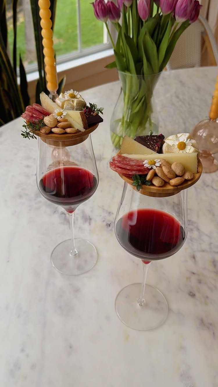 Wine glasses topped with charcuterie platters featuring cheese and salami on marble table