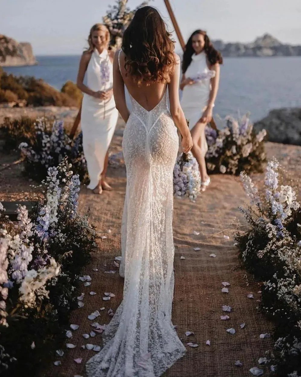 Bride in lace gown walking barefoot on burlap runner toward bridesmaids at beach wedding