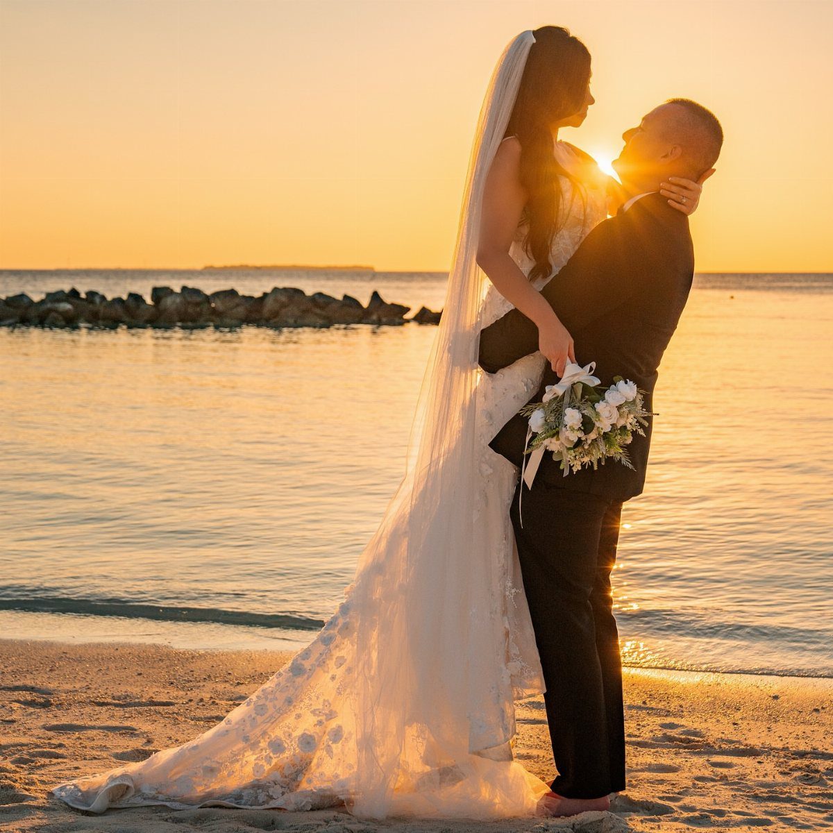 Bride and groom embracing on a sandy beach during a golden sunset.