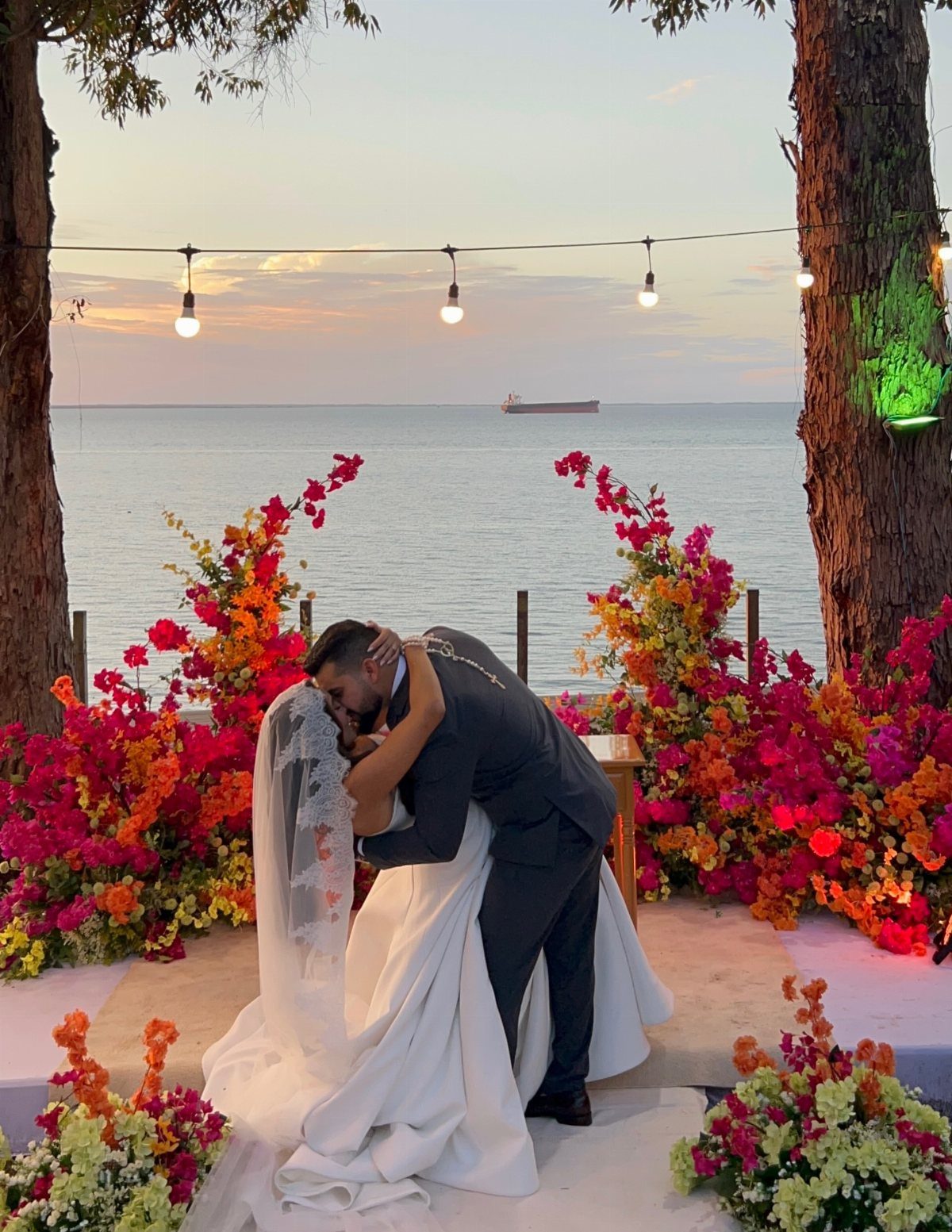 Bride and groom kissing at a floral beach altar during a sunset wedding.