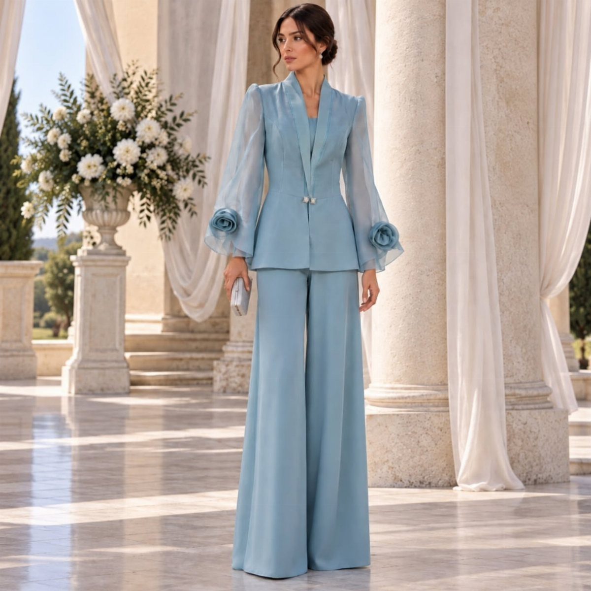 Woman in a light blue blazer and wide-leg trousers standing by white columns.