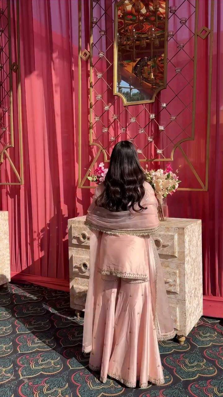 Woman in light pink traditional Indian outfit standing before a white dresser.