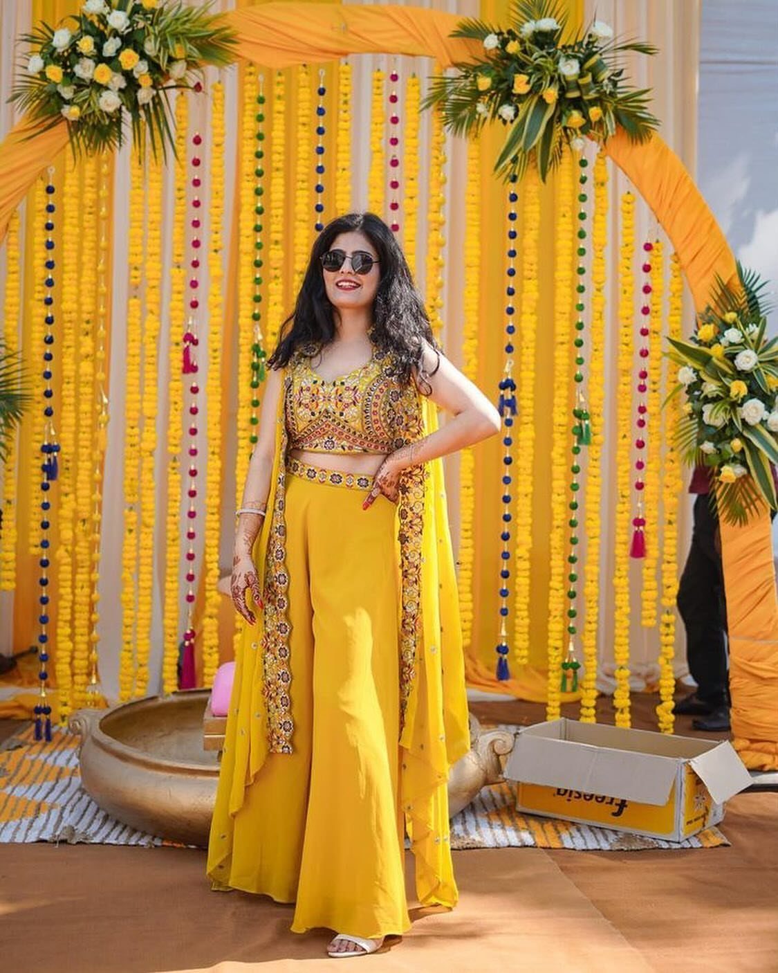 Woman in yellow embellished co-ord set with wide-leg trousers and a matching cape.