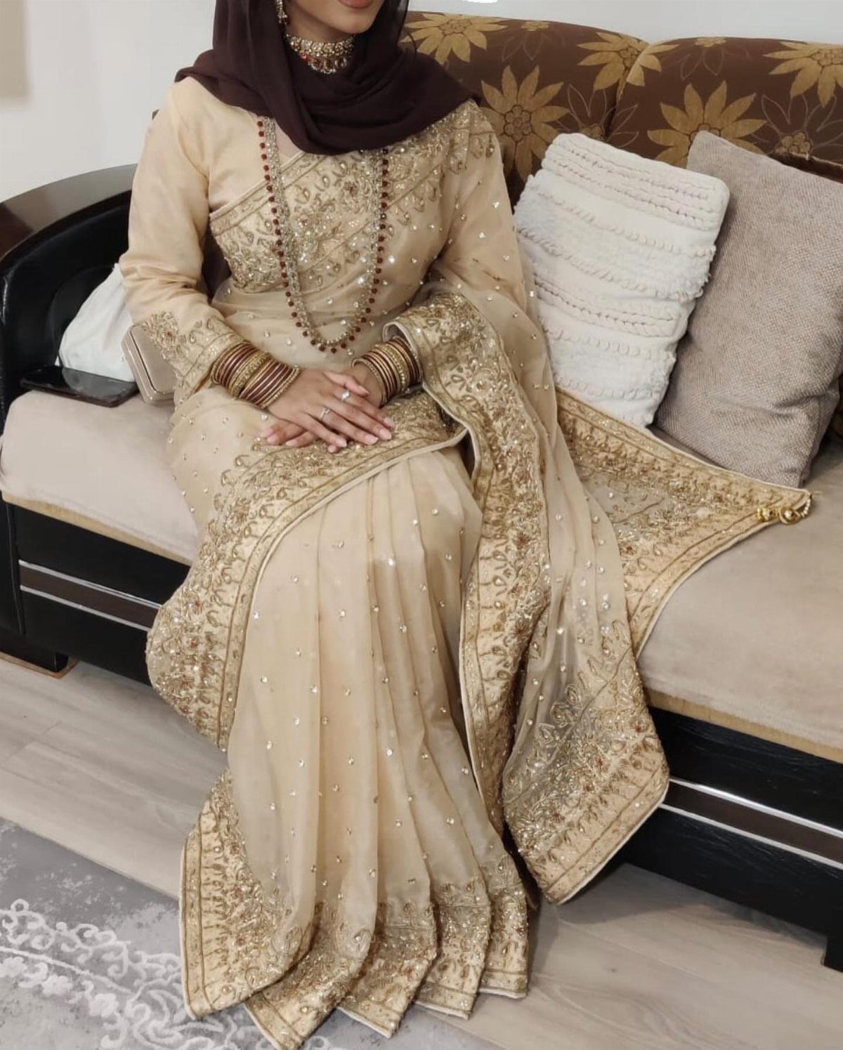 Woman in a beige embellished sari with gold embroidery and a brown hijab.