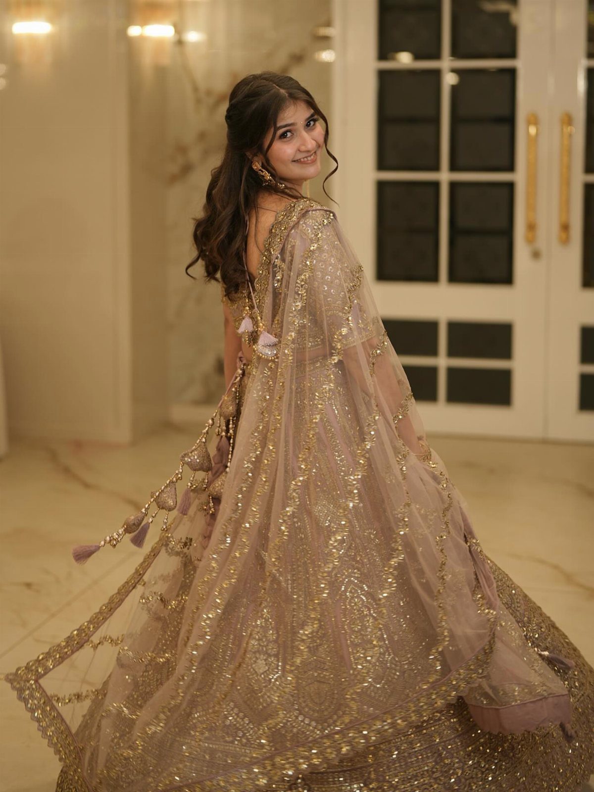 Woman wearing a heavily embellished gold lehenga with a matching sheer dupatta.
