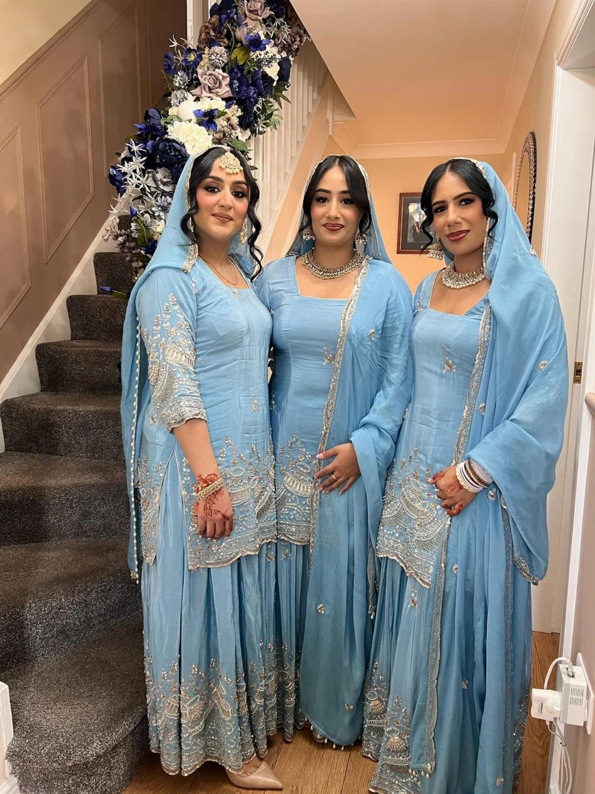 Three women wearing matching ice blue embroidered kurta sets with silver shimmer details.
