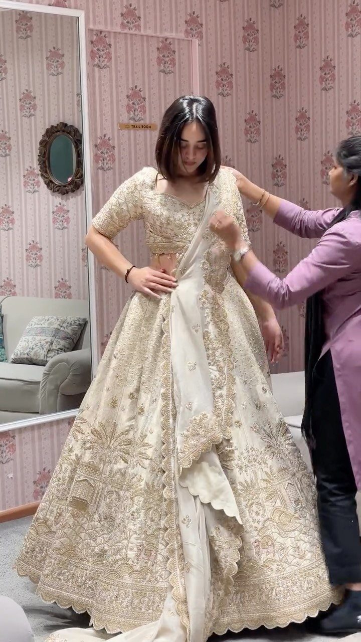 Woman wearing an ivory wedding lehenga with gold embroidery in a floral room.
