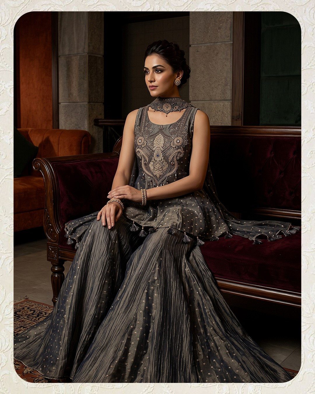 Woman in a metallic grey embellished lehenga sitting on a red velvet sofa.