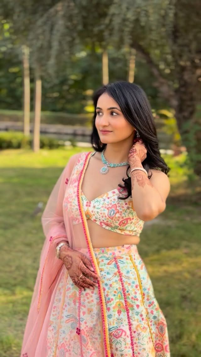 Woman in a pastel floral lehenga with a pink dupatta posing in a garden.