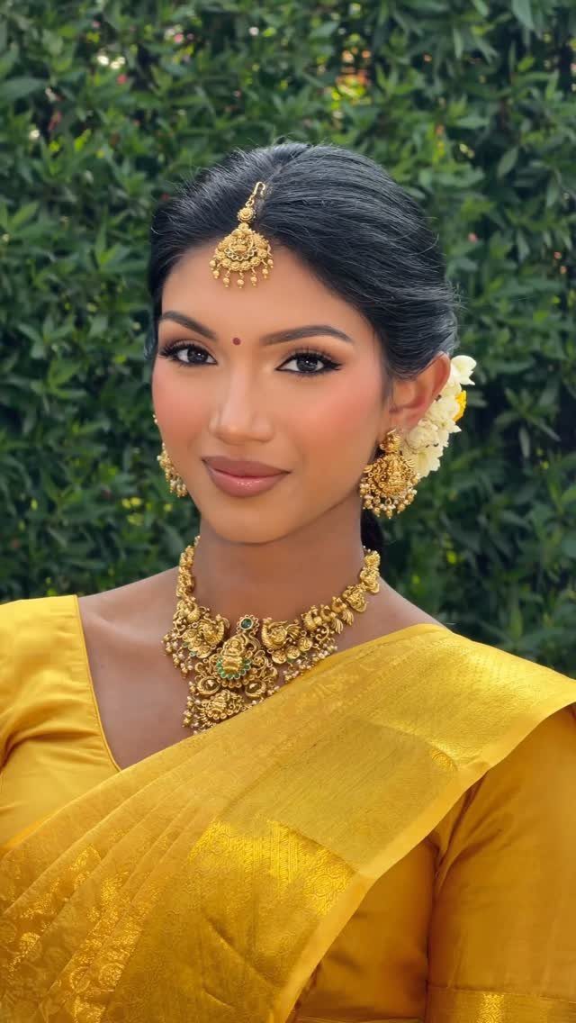 Woman in a bright yellow silk saree with gold jewelry and white flowers.