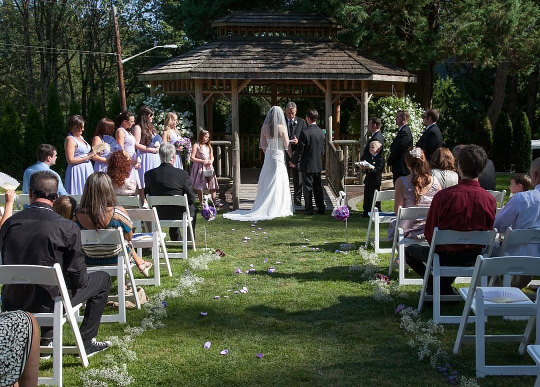 Wedding ceremony with guests seated on a lawn before a wooden gazebo