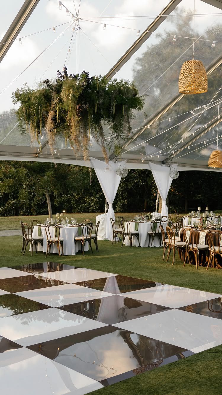 Clear marquee tent with dining tables and a checkered dance floor on green grass