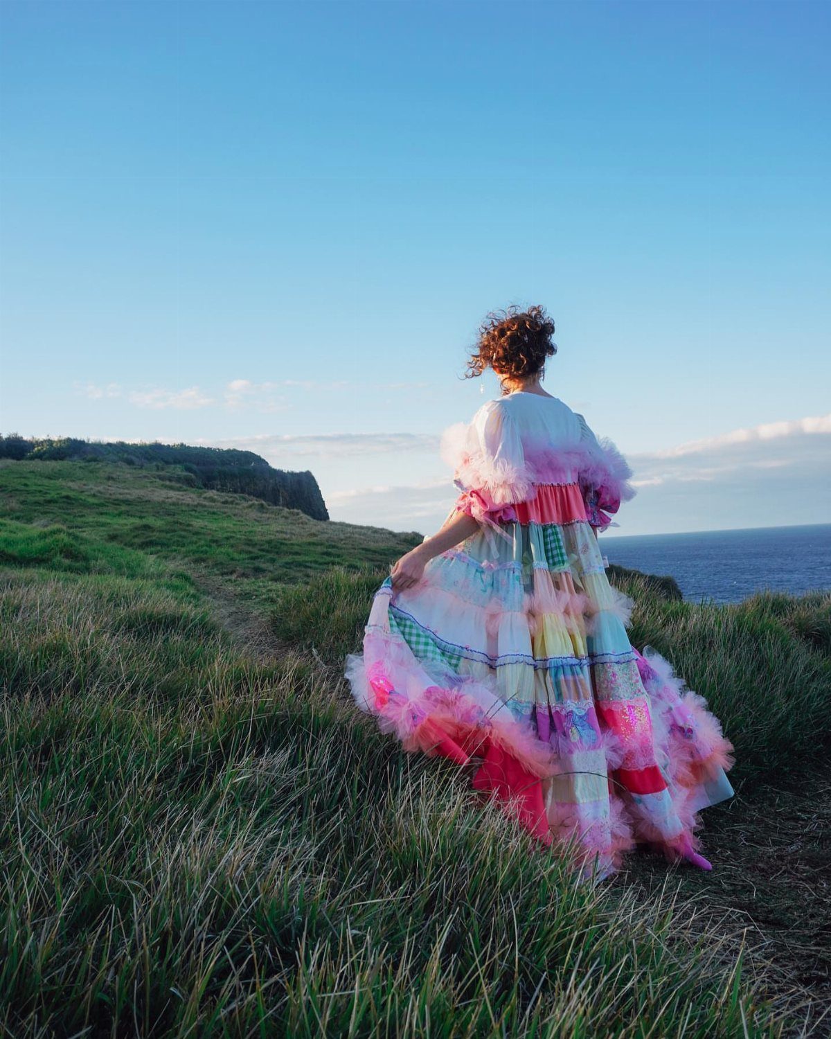 Claire Wedding Dress Styles: 11 Gowns to Inspire Your Look 7 Woman in a colorful ruffled gown standing on a grassy cliff by the sea