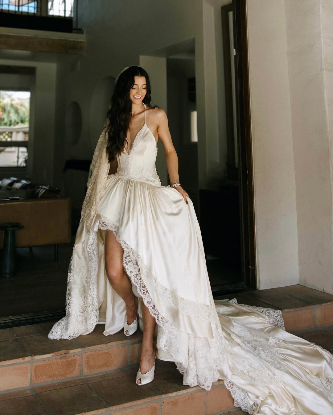 Claire Wedding Dress Styles: 11 Gowns to Inspire Your Look 11 Woman in a white satin wedding dress with lace trim on terracotta steps.