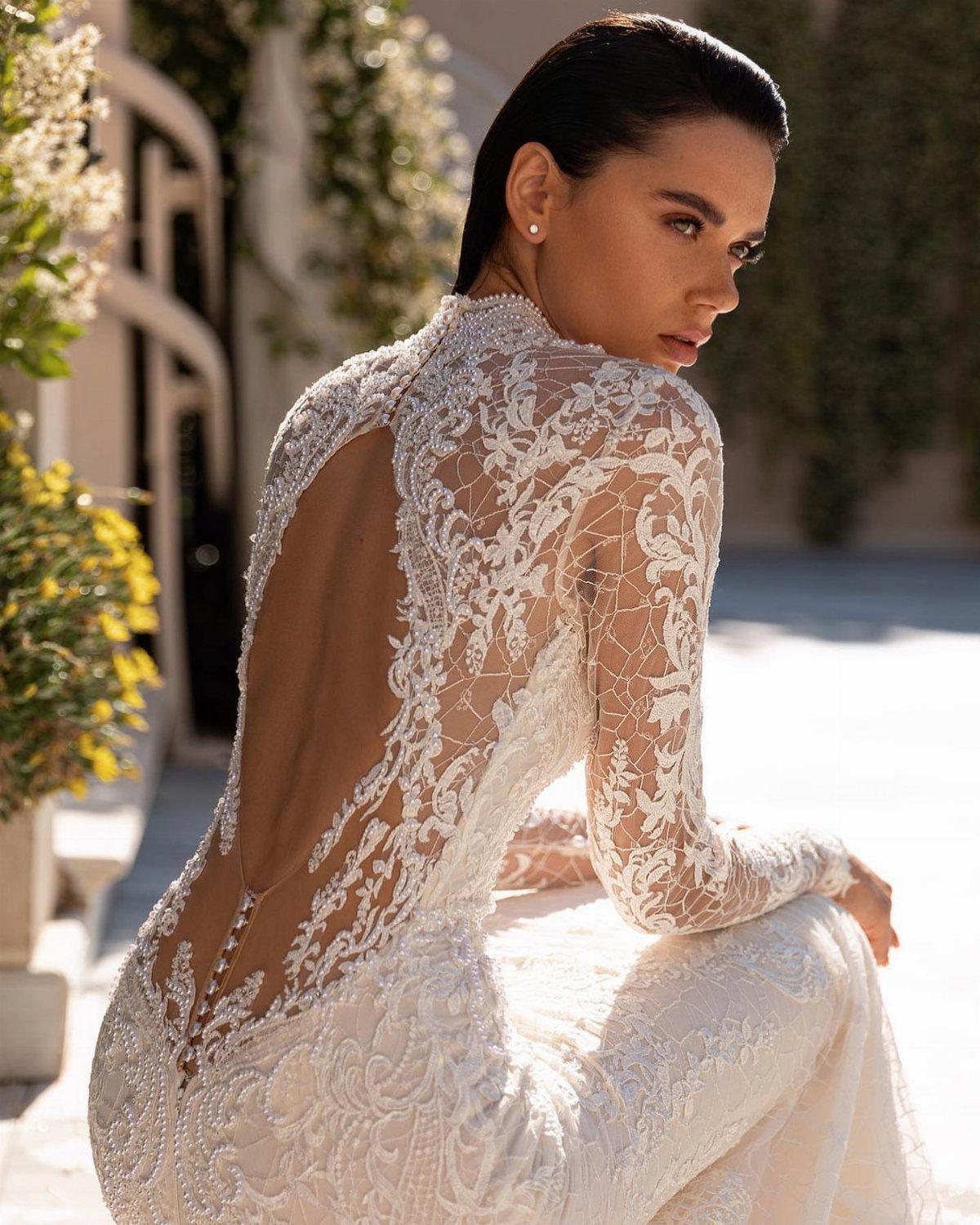 Claire Wedding Dress Styles: 11 Gowns to Inspire Your Look 2 Woman in a long-sleeved white lace wedding gown with an open back.