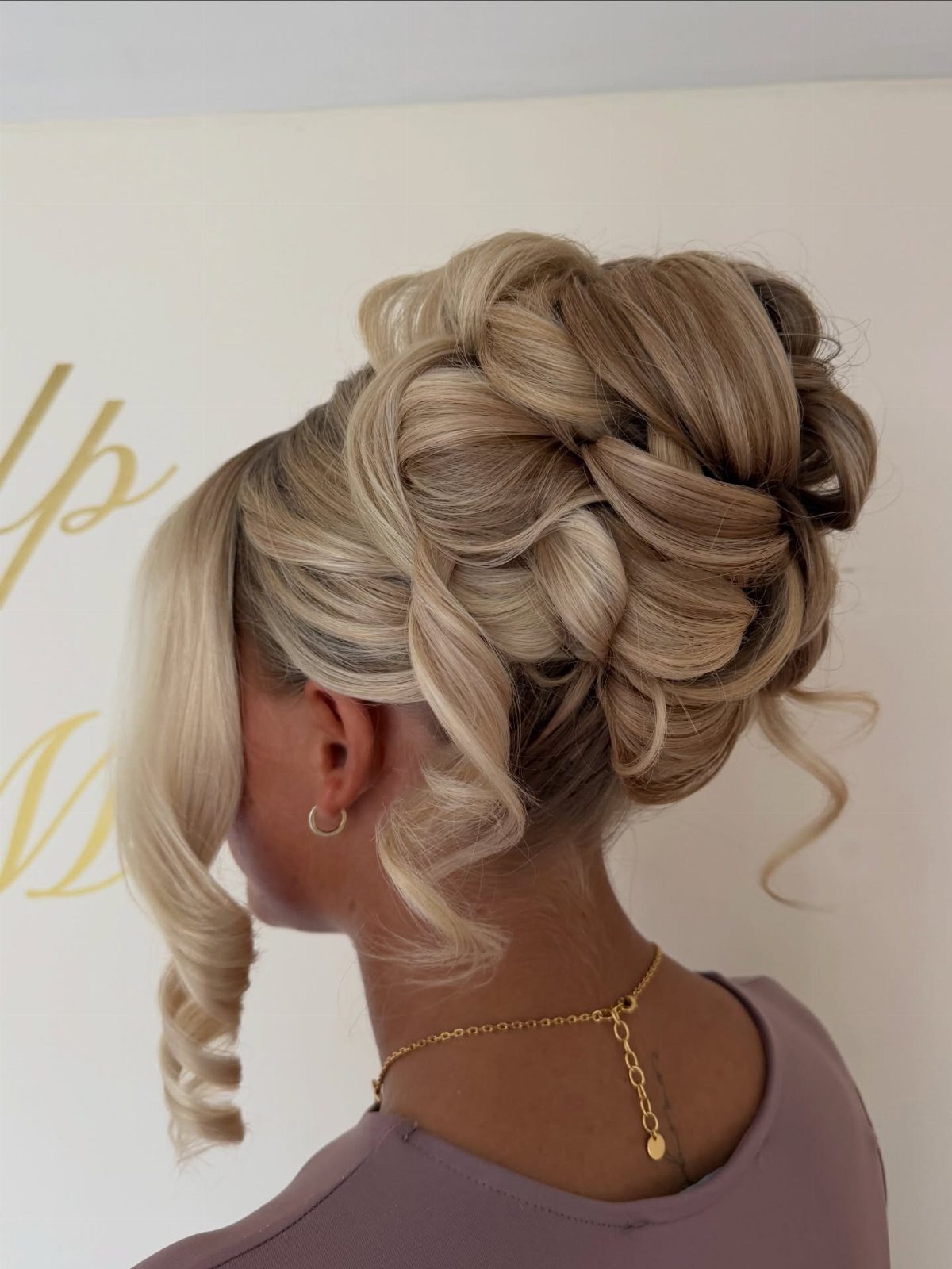 Blonde woman with an intricate curly wedding updo and loose face-framing tendrils.