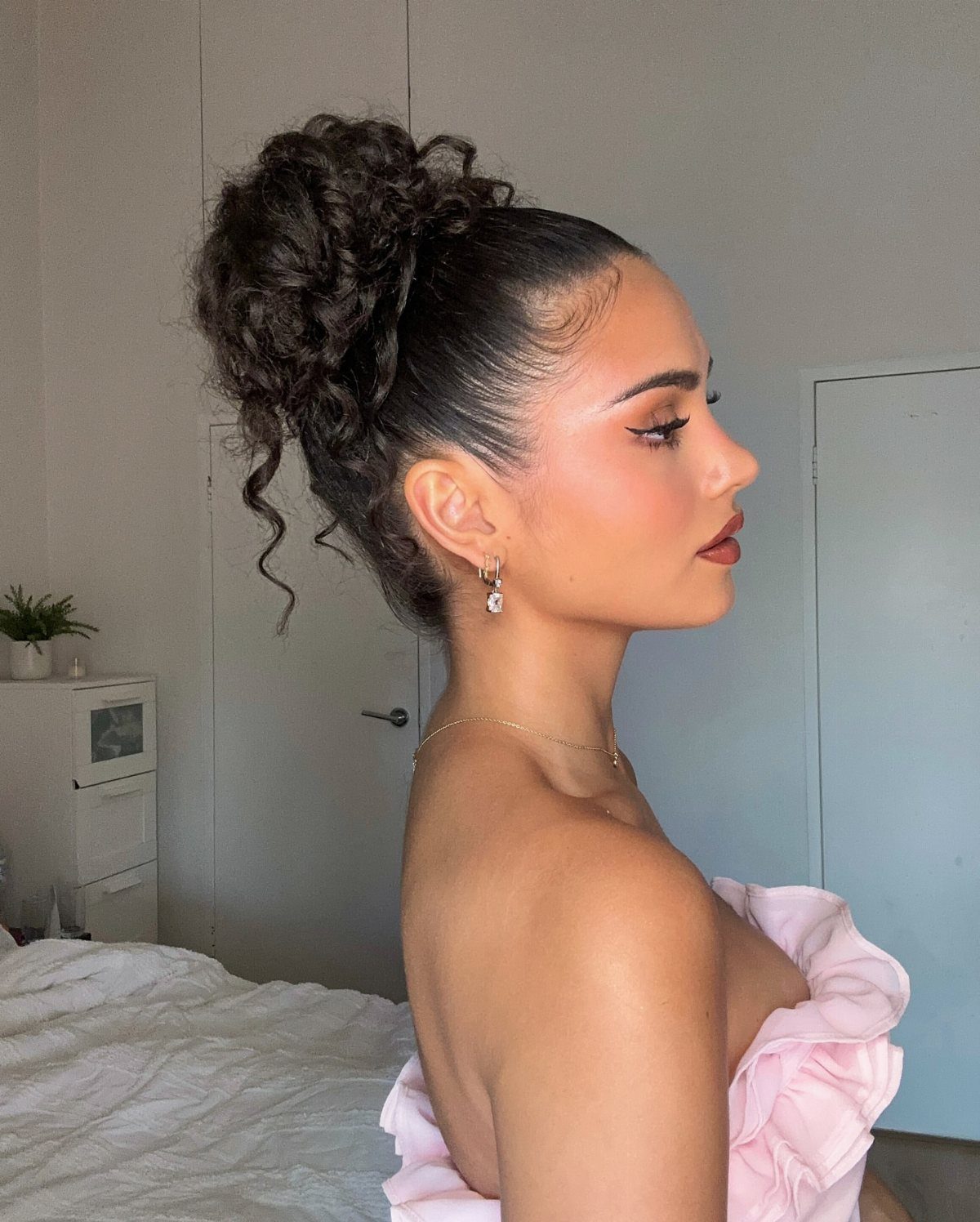 Woman with a high voluminous curly bun updo and pink ruffled dress.