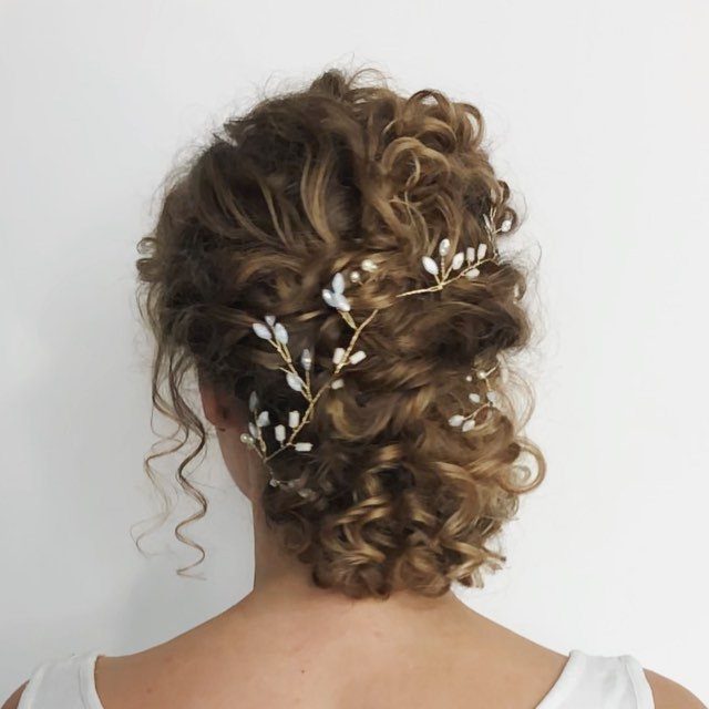 Curly brown hair styled in an updo with a gold and white hairpiece.
