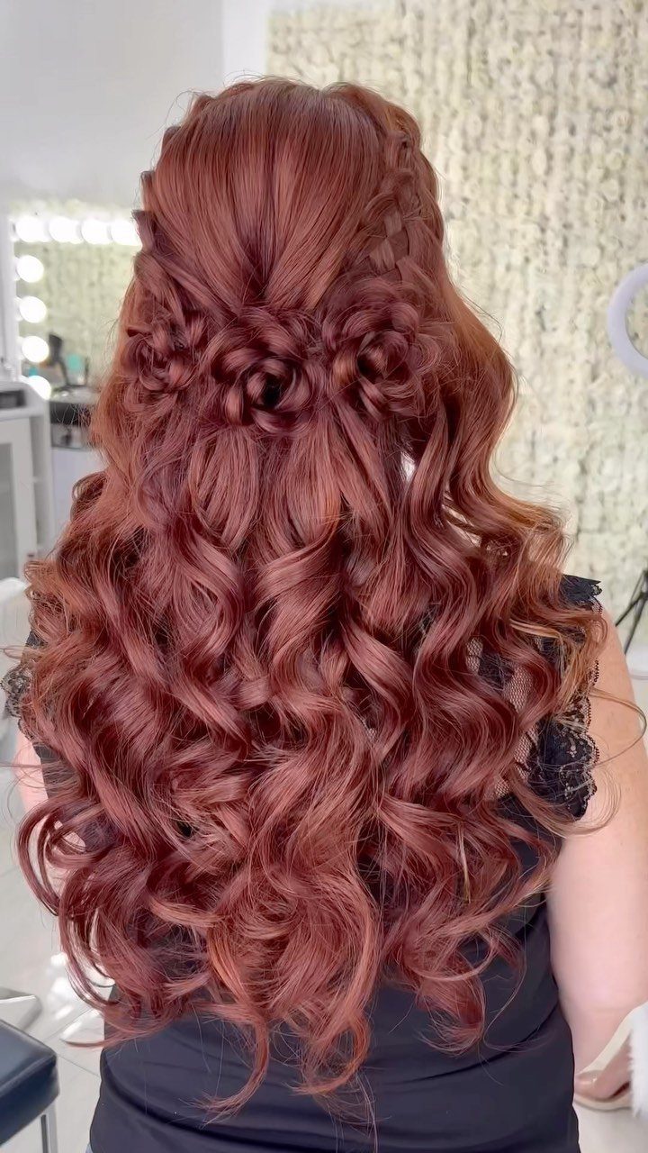 Reddish-brown curly hair styled in a half-updo with a braided knot back.