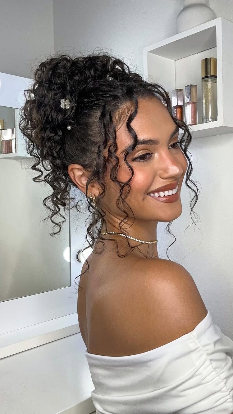 Woman with dark curly hair in a high wedding updo and white top.