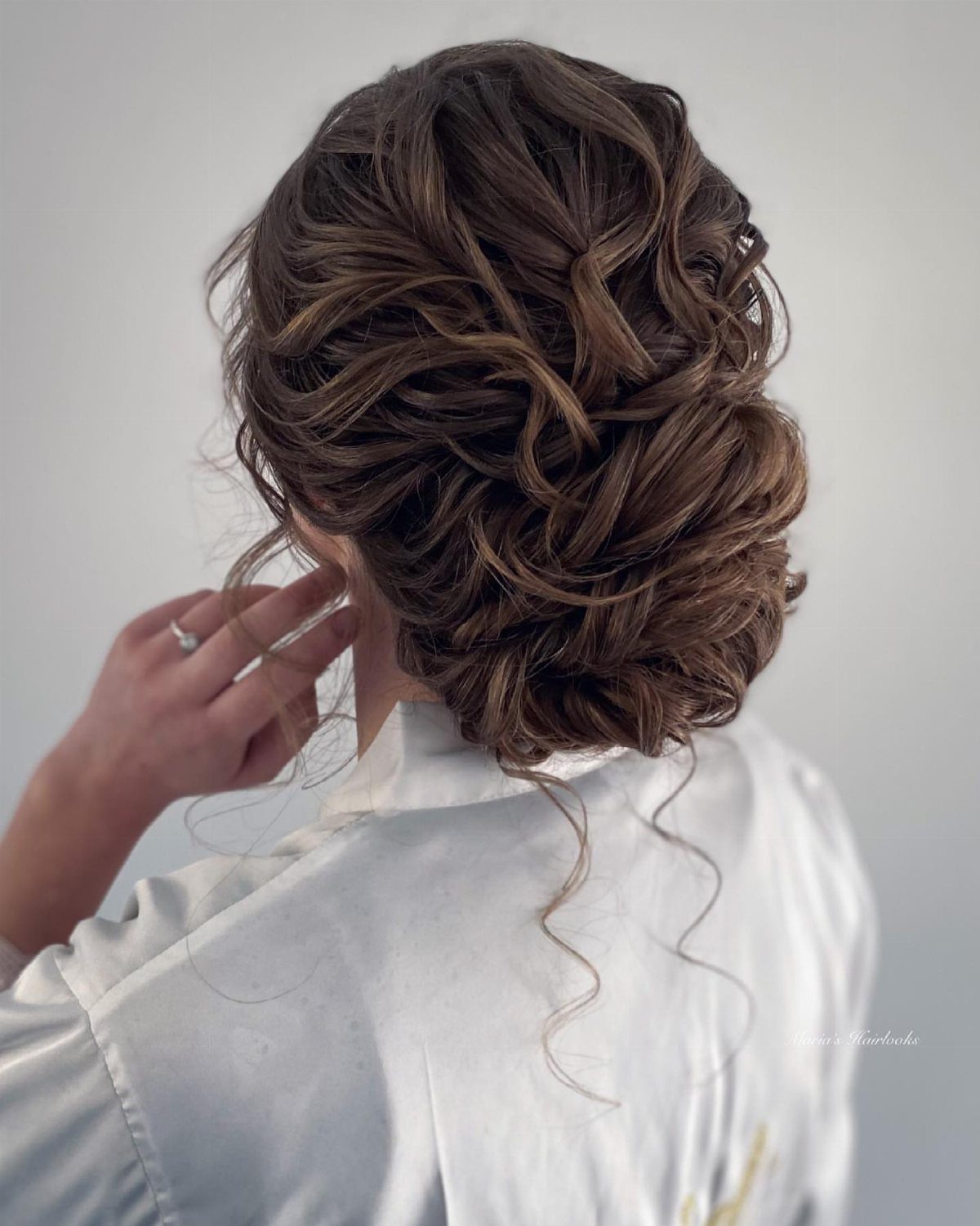 Brown curly hair styled in a voluminous low bun with loose face-framing tendrils.