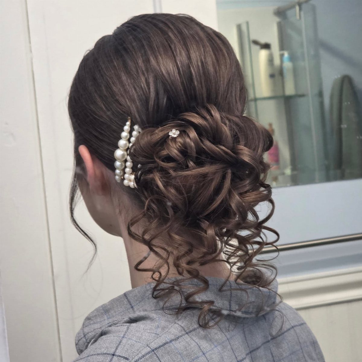 Brown curly updo with a row of white pearl pins and a sparkling jewel.