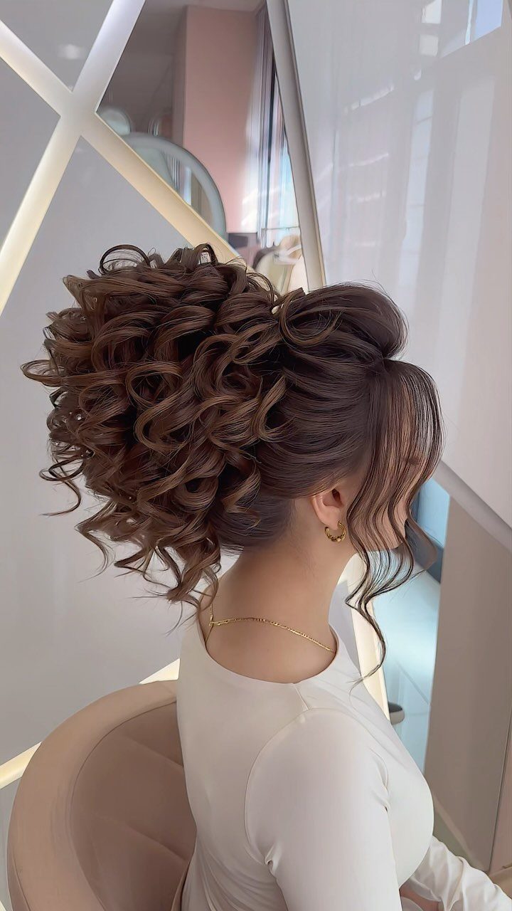 Voluminous brown curly updo with a high bun and face-framing curls on a woman.