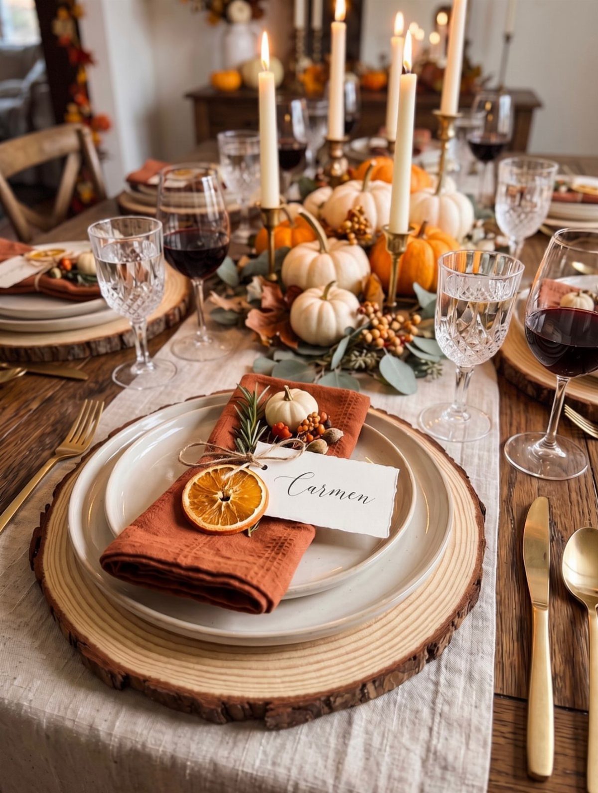Rustic autumn table setting with white pumpkins, lit candles, and red wine glasses.