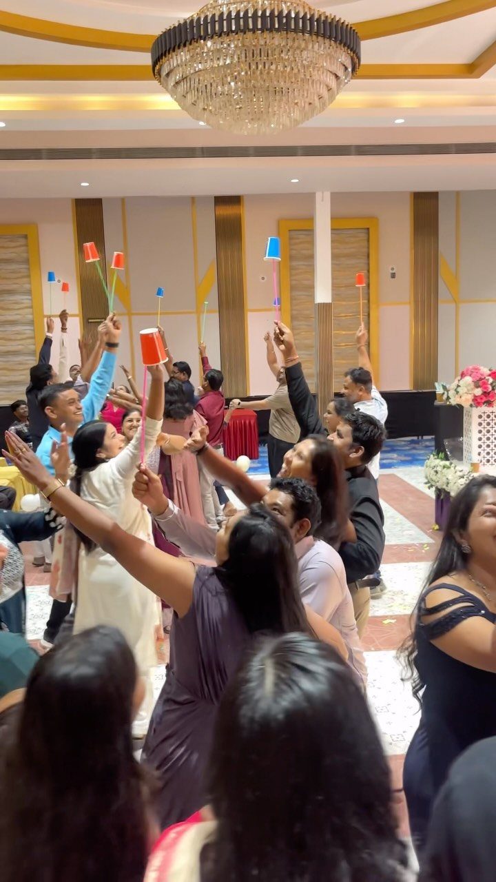 People holding colorful plastic cups on sticks in a formal indoor ballroom setting.
