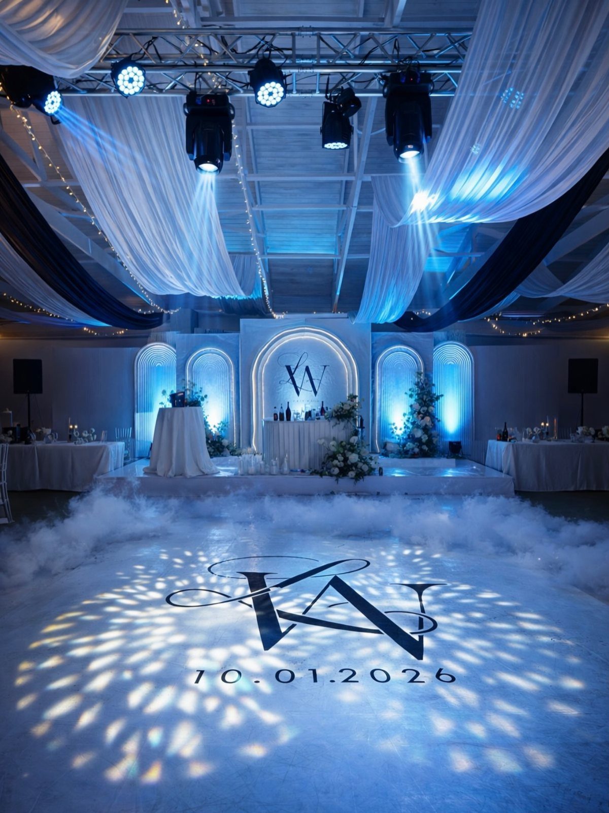 Wedding reception dance floor with blue lighting, white drapes, and a projected monogram.