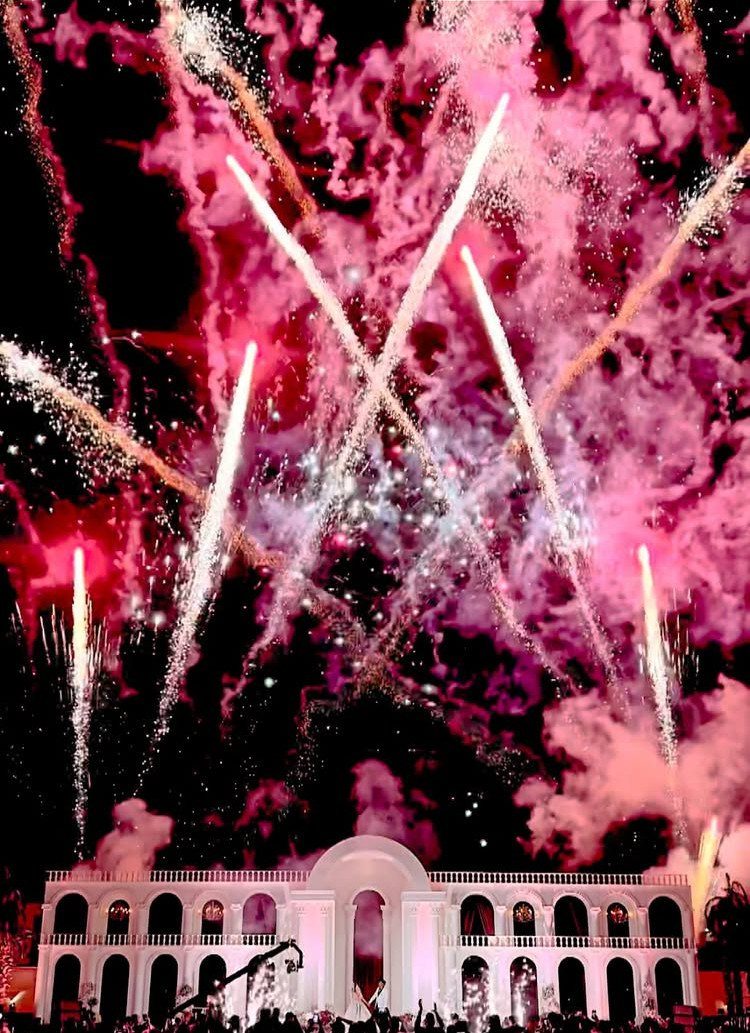 Pink and white fireworks exploding in the night sky over a white building.