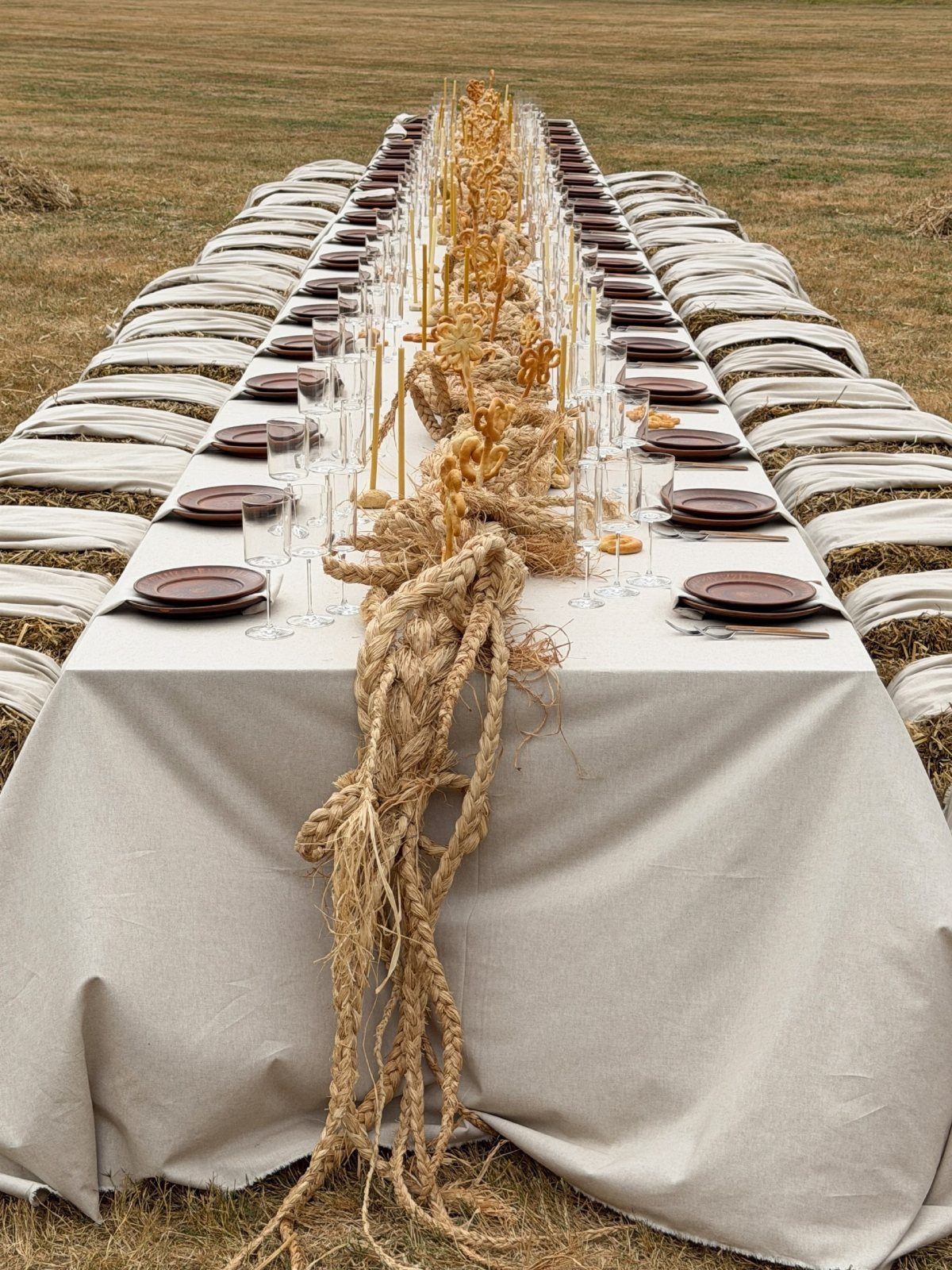 Long outdoor dining table with rope runner, dried wheat, and hay bale seating.