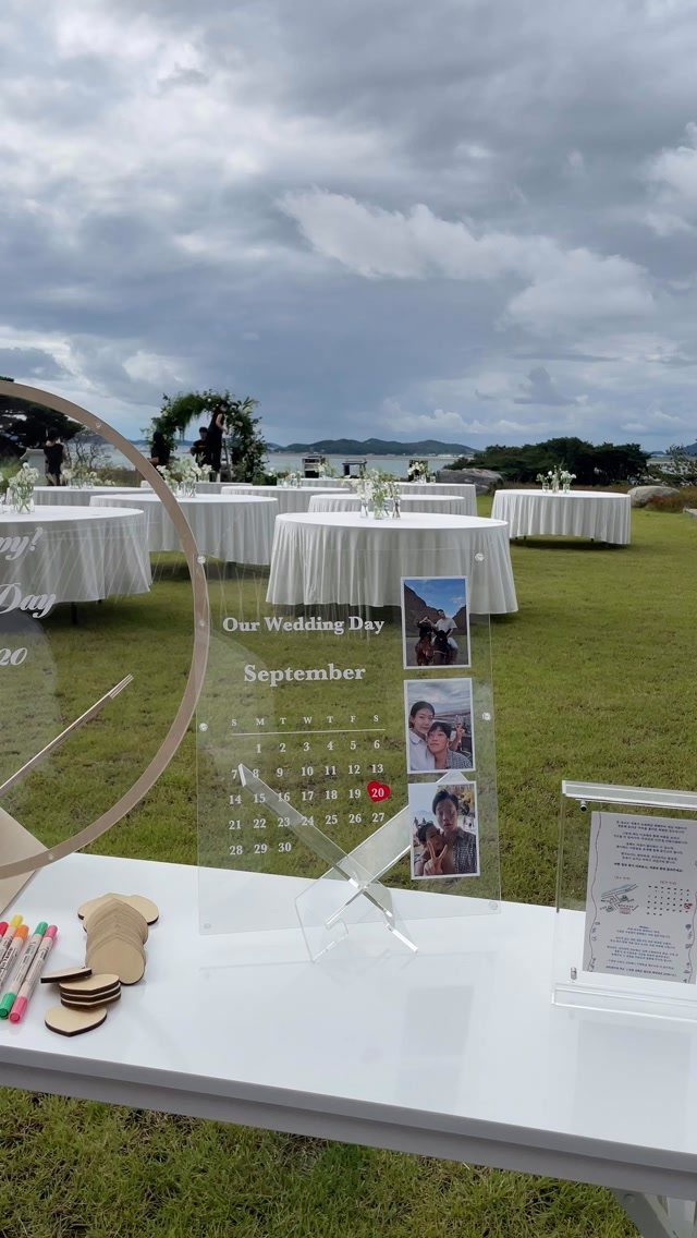 Acrylic wedding calendar sign with photos on a white table at outdoor reception