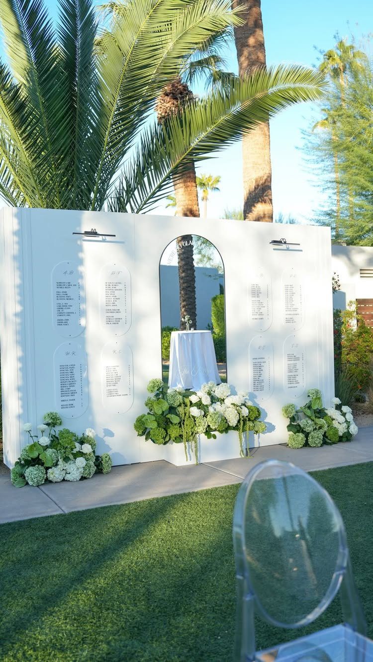 White wedding seating chart wall decorated with green and white hydrangeas outdoors.