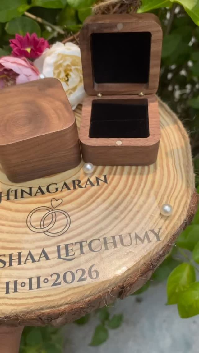 Wooden tree slice platter with engraved names, ring boxes, and floral decorations.
