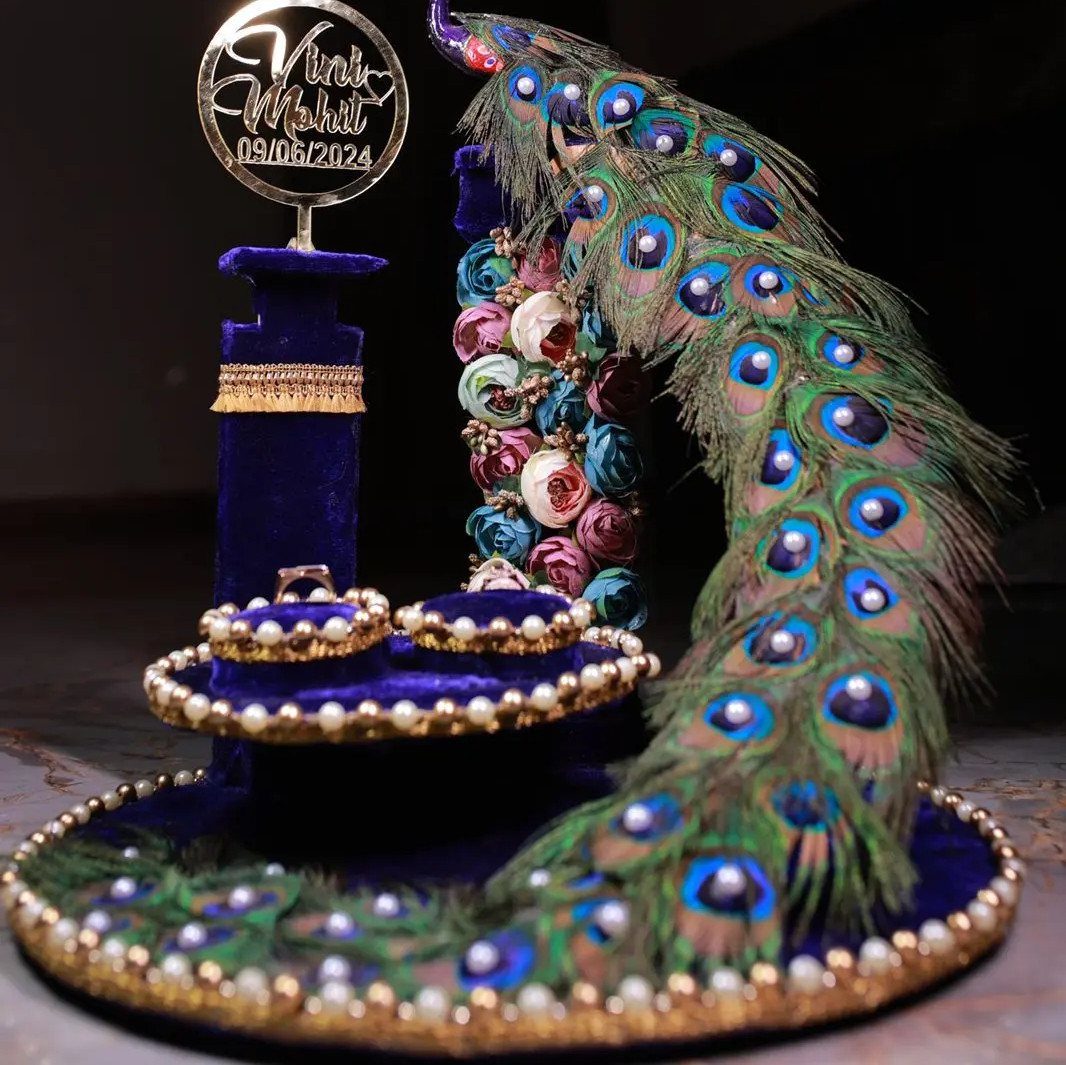 Blue velvet engagement ring tray with peacock feathers, fabric roses, and a gold name topper.