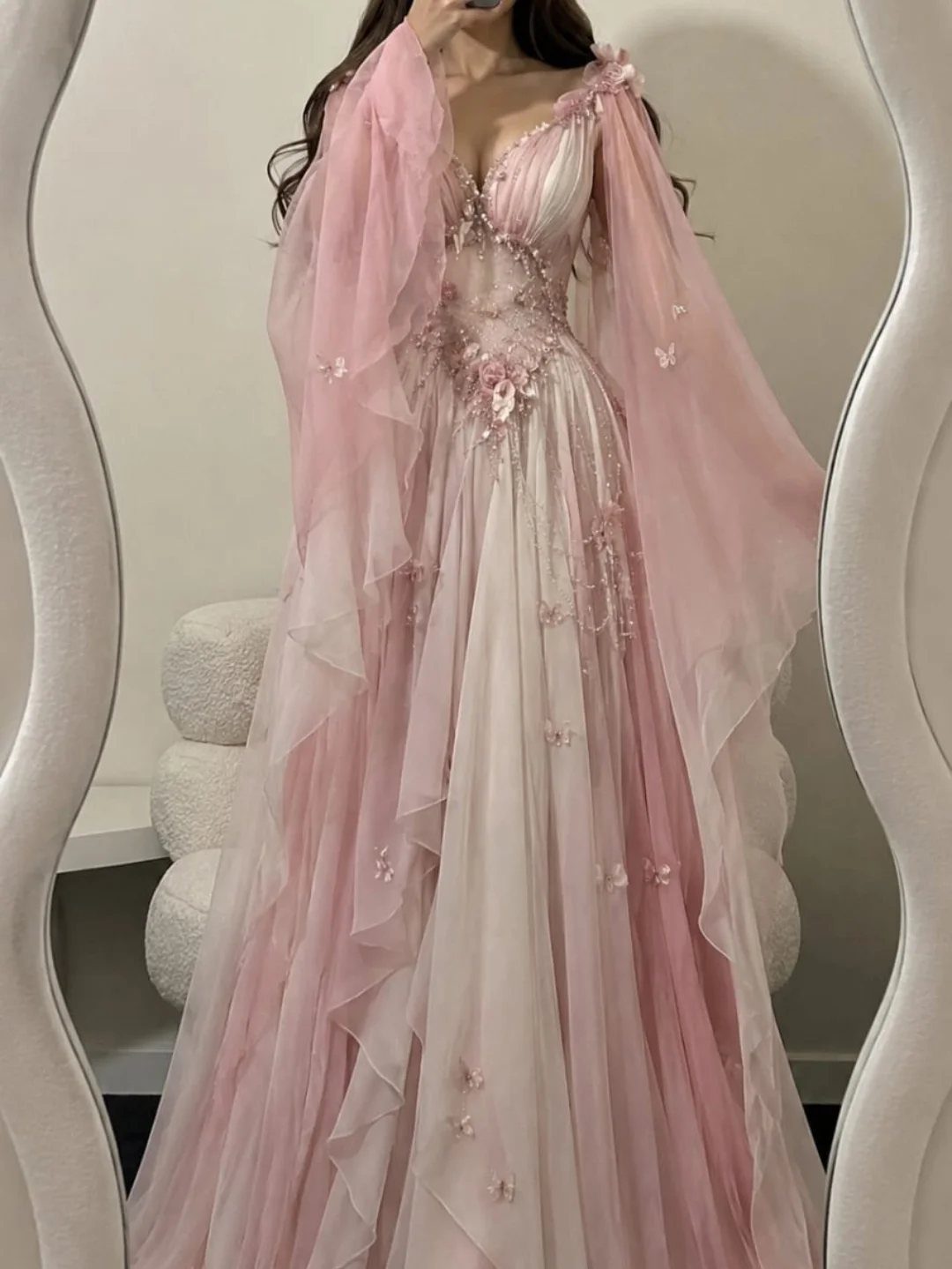 Pink layered gown with floral embroidery and sheer sleeves on a person.