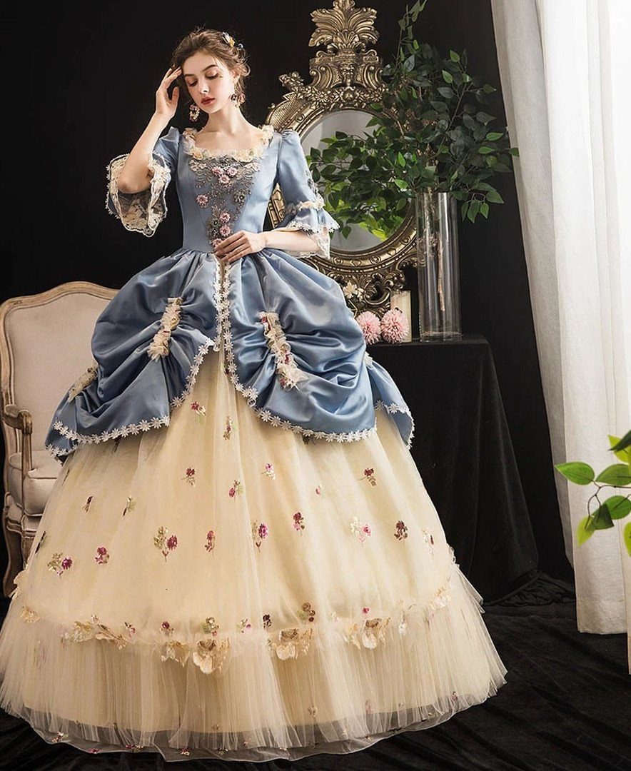 Woman in a blue and cream ballgown with floral embroidery and voluminous tulle skirt.
