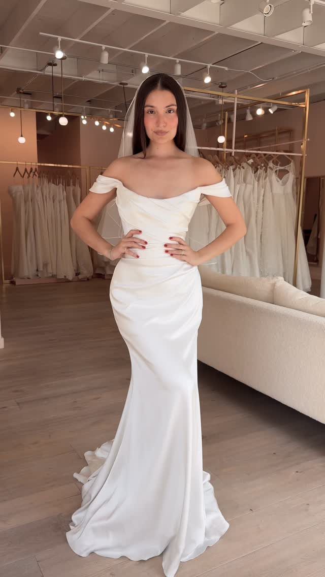 Woman in a white off-the-shoulder fit-and-flare wedding dress posing in a bridal shop.