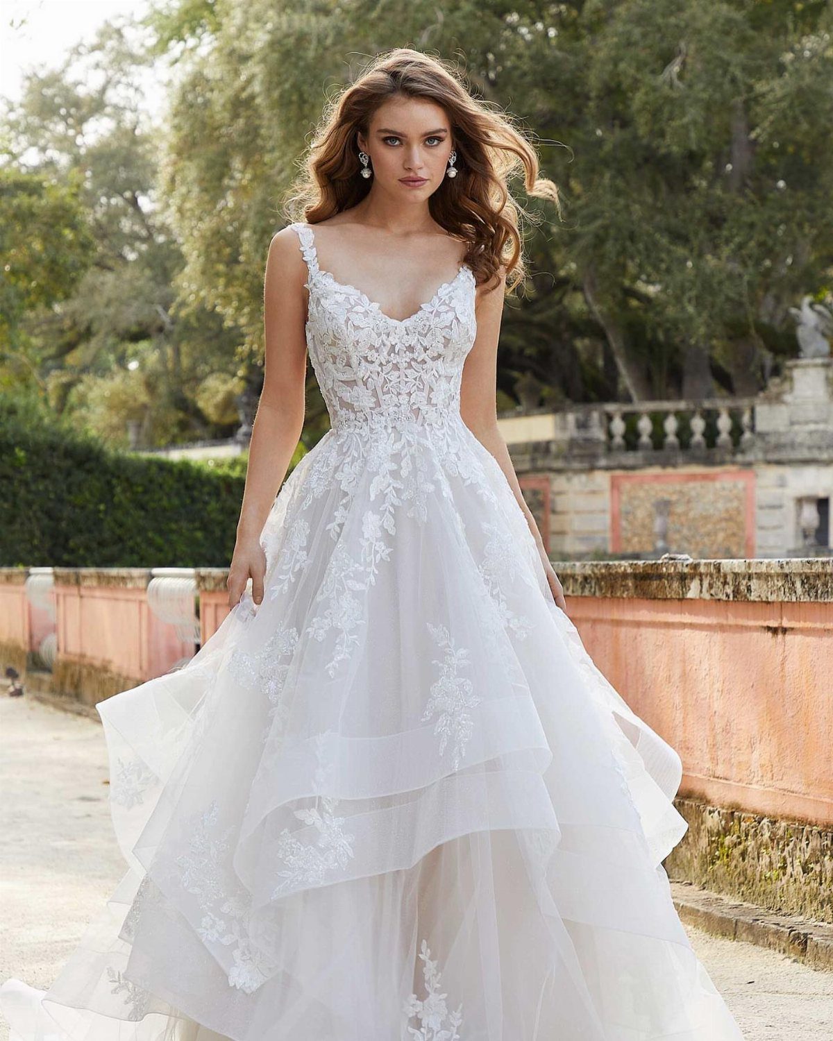 Woman in a white layered lace wedding dress posing in a sunny garden.